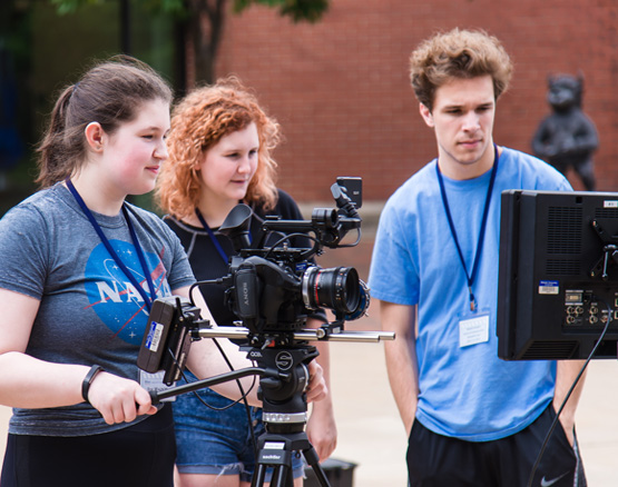 Three students work on a film production set.