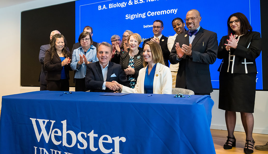 Webster University and Barnes-Jewish College officials shake hands on stage